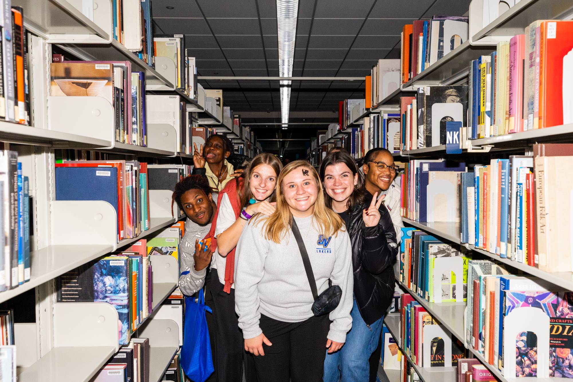 group of students standing in between two library stacks full of books
